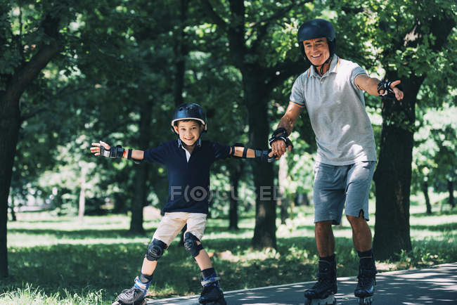 Grandfather and grandson enjoying rollerskating in summer park. — Stock Photo