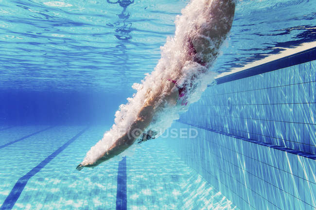 Female swimmer diving into public swimming pool water. — Stock Photo