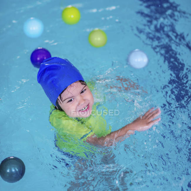 Toddler boy in blue cap learning swimming in swimming pool. — Stock Photo