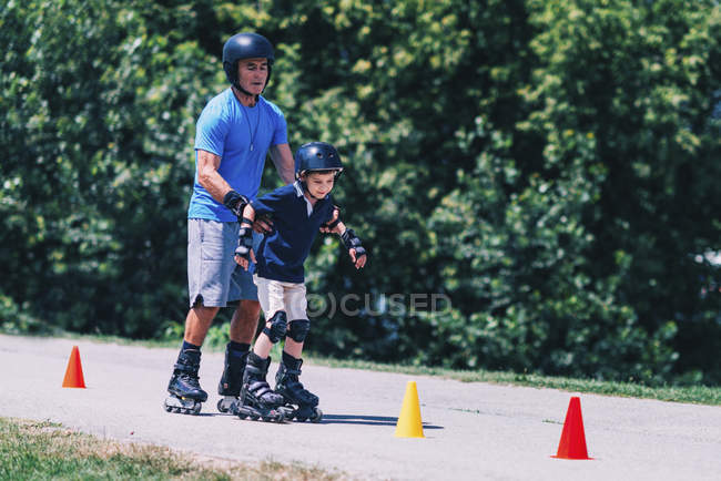 Profesor sénior de patinaje sobre ruedas con niño practicando en clase en el parque . - foto de stock