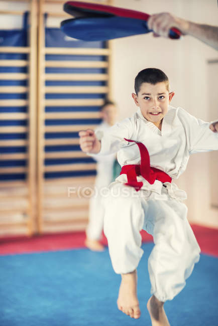 Menino da idade elementar pulando na aula de taekwondo com treinador . — Fotografia de Stock