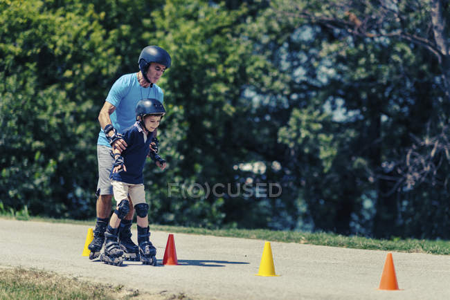 Professor sênior de rollerskating com menino praticando em classe no parque . — Fotografia de Stock
