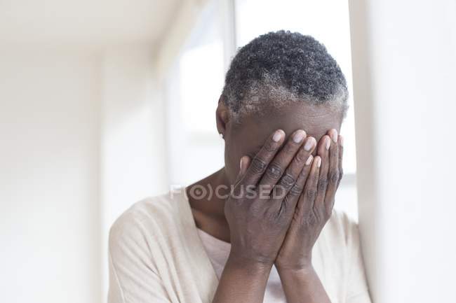 Mature woman with head in hands indoors. — Stock Photo