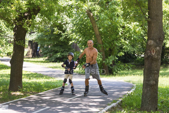 Grandfather teaching grandson rollerskating outdoors. — Stock Photo