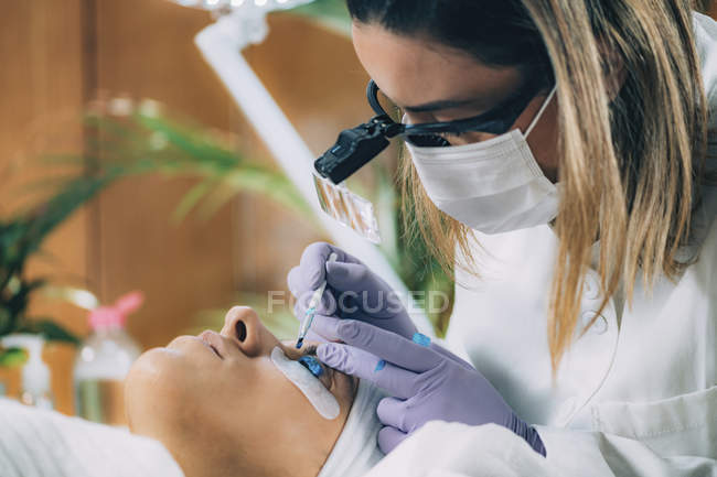 Cosmetologist putting blue paint on patient eyelashes during lash lifting and laminating procedure. — Stock Photo