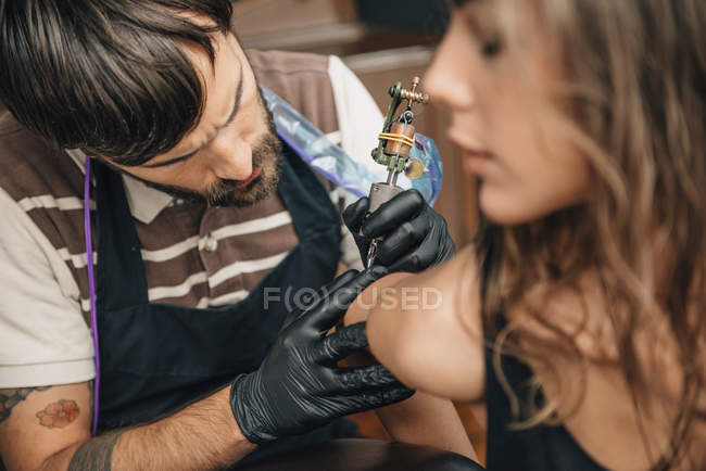 Tattooist focused on tattoo work on female client. — Stock Photo