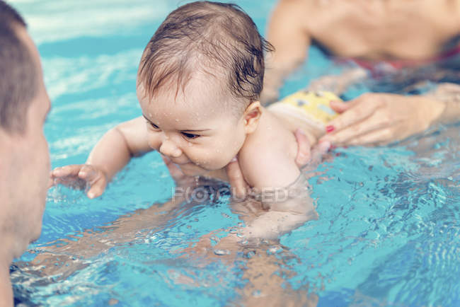 Милый мальчик плавает с инструктором и матерью в бассейне воды . — стоковое фото