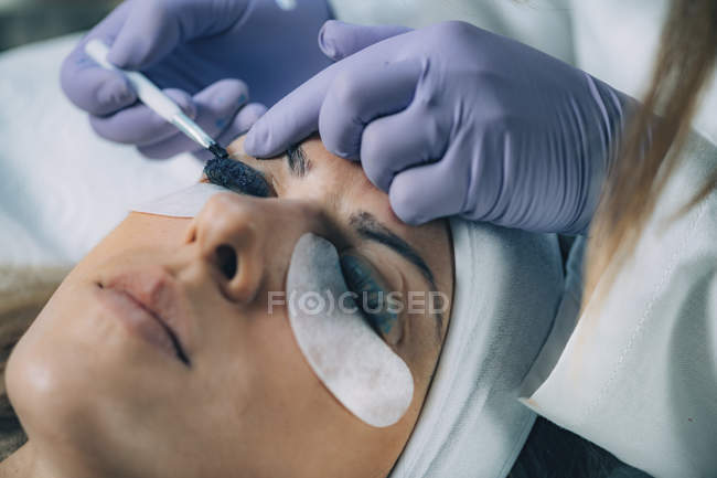 Cosmetologist colocando tinta preta nas pestanas do paciente durante o procedimento de elevação e laminação das pestanas . — Fotografia de Stock