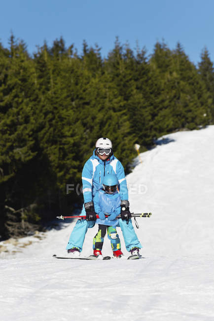 Little boy in winter clothing learning skiing with father at snowy resort. — Stock Photo