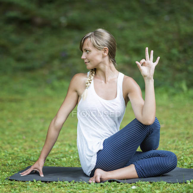 Donna che pratica torsione con segno mano mudra yoga sul tappeto nel parco . — Foto stock