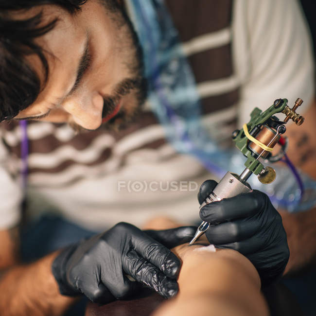 Maestro tatuando la piel femenina en detalle en el estudio . - foto de stock