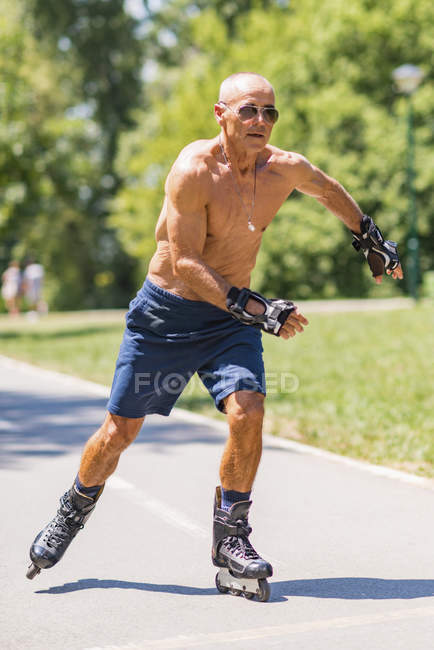 Shirtless senior hombre patinaje sobre ruedas en el parque en verano . - foto de stock