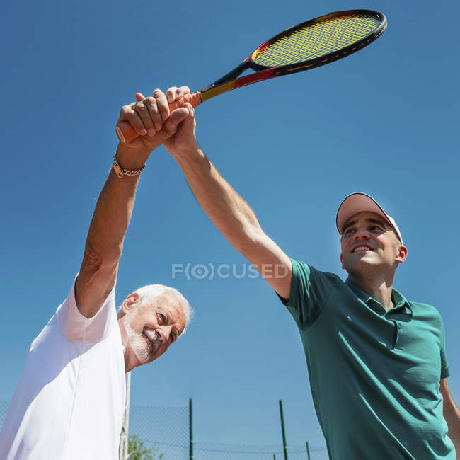Тенісний інструктор, що практикує з старшим чоловіком на уроці тенісу . — стокове фото