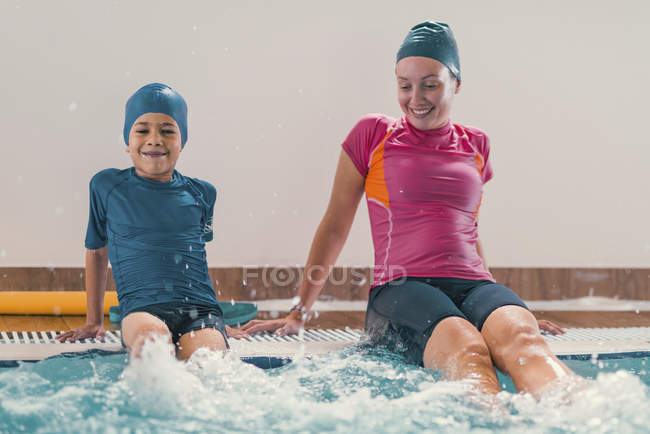 Niño en clase de natación con instructor en piscina pública . - foto de stock