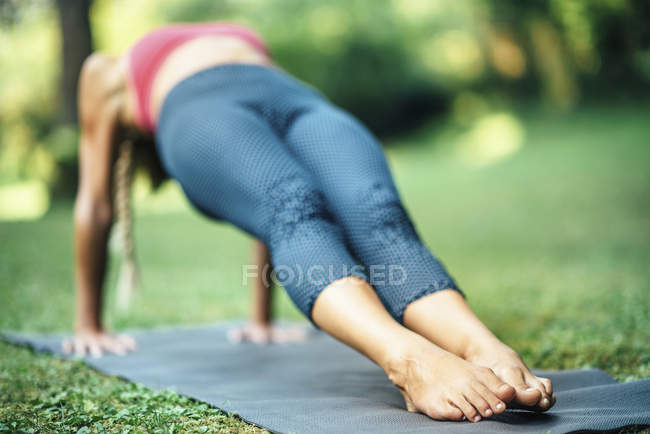 Жінка робить йогу і стоїть в оберненій дошці позу пурвотанана на килимку в парку . — стокове фото