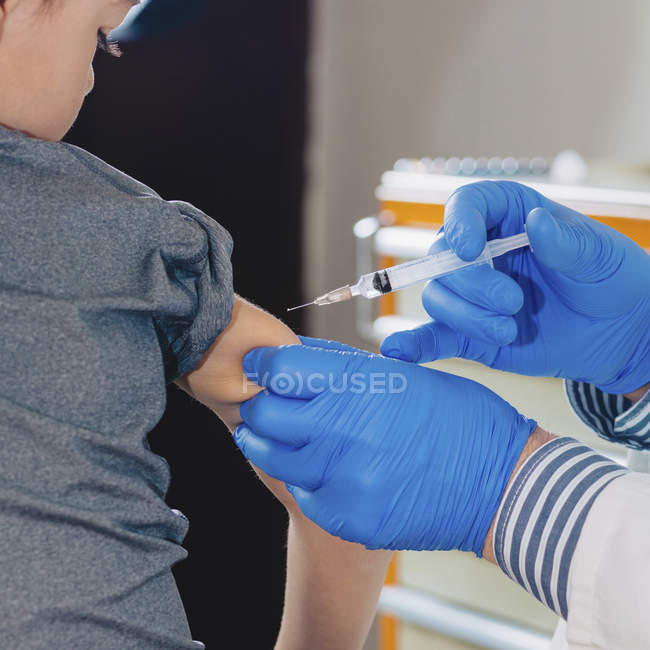 Elementary age boy receiving syringe vaccination in medical clinic. — Stock Photo