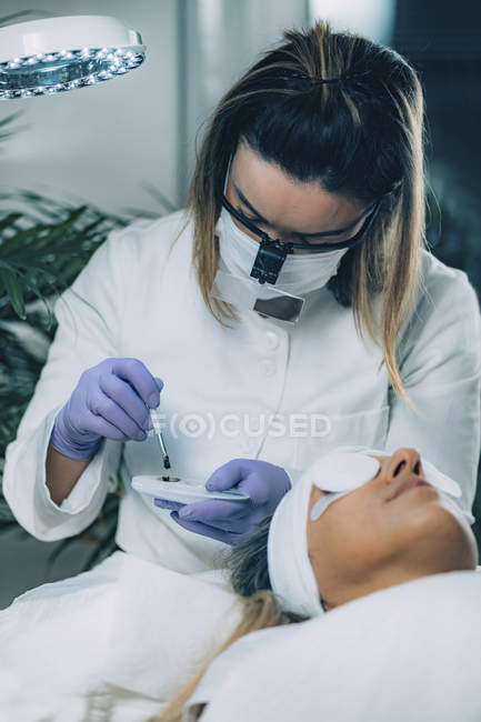 Cosmetologist putting black paint on patient eyelashes during lash lifting and laminating procedure. — Stock Photo