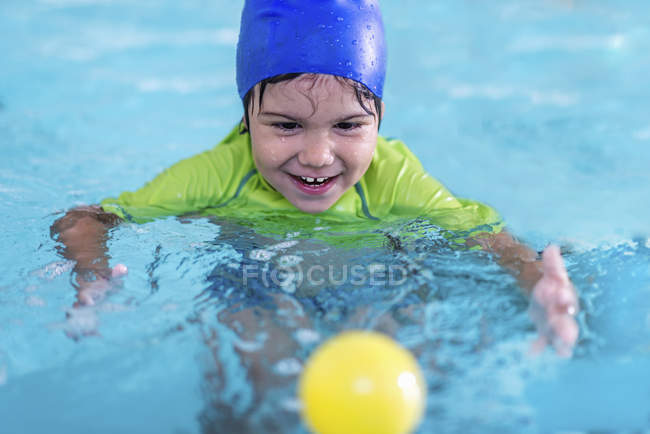 Toddler boy in blue cap playing with ball in swimming pool. — Stock Photo