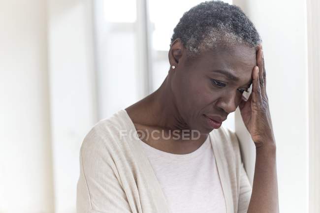 Mature woman touching forehead with pensive expression. — Stock Photo