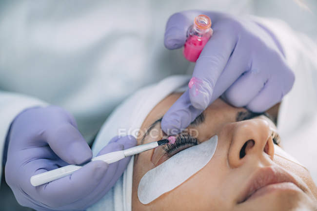 Cosmetologist putting pink paint on patient eyelashes during lash lifting and laminating procedure. — Stock Photo