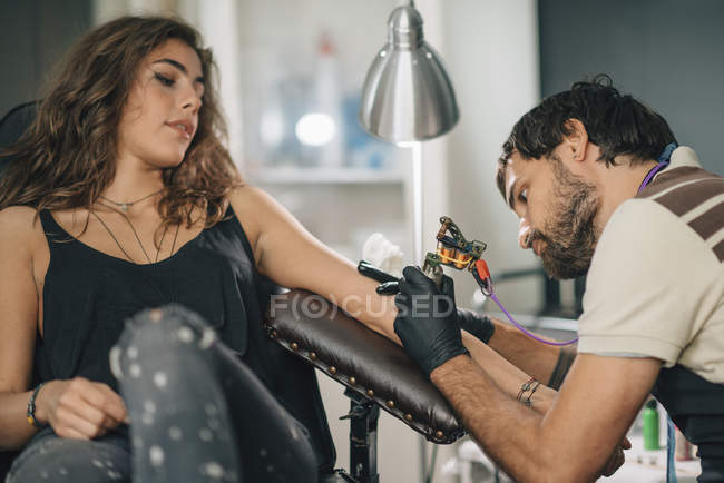 Tattooist focused on tattoo work on female client. — Stock Photo