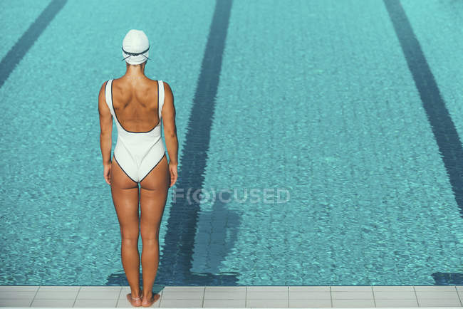 Rear view of female swimmer standing on poolside. — Stock Photo