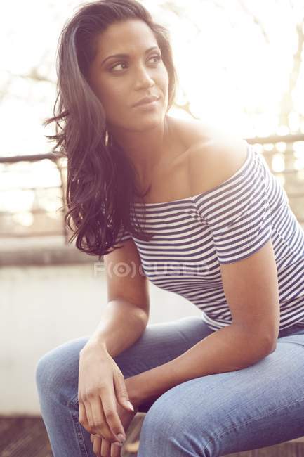 Femme de race mixte adulte moyenne assise à l'extérieur et regardant ailleurs, portrait . — Photo de stock