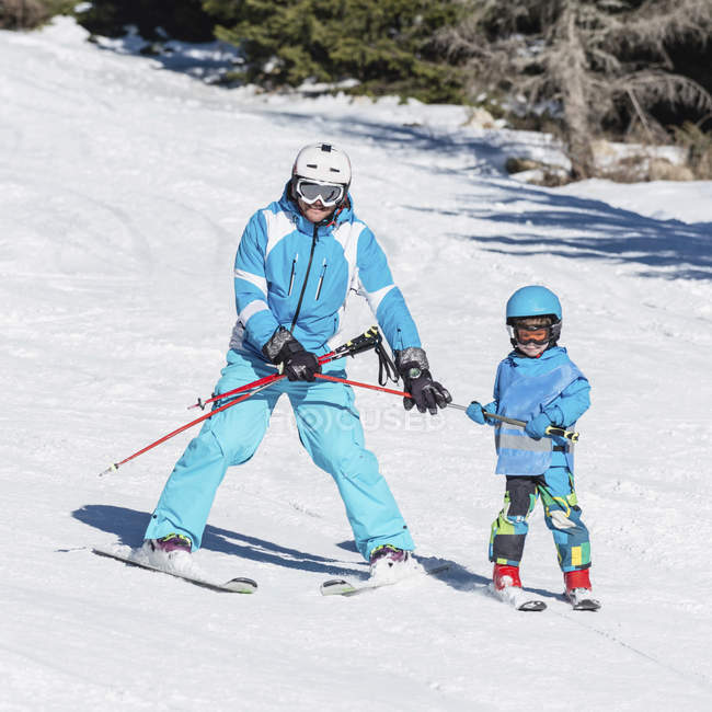Little boy in winter clothing learning skiing with father at snowy resort. — Stock Photo