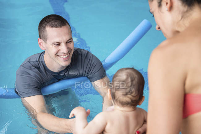 Instructor with water noodle with baby boy and mother playing in pool. — Stock Photo