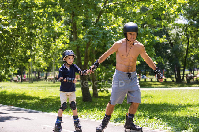 Abuelo enseñando a su nieto a patinar en el parque . - foto de stock