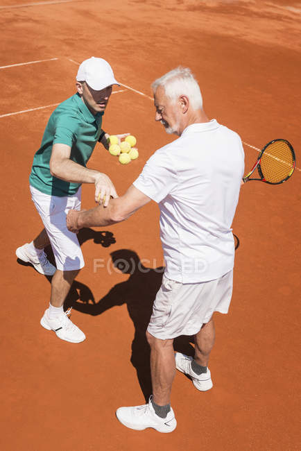 Senior activo practicando en clase de tenis con instructor masculino . - foto de stock