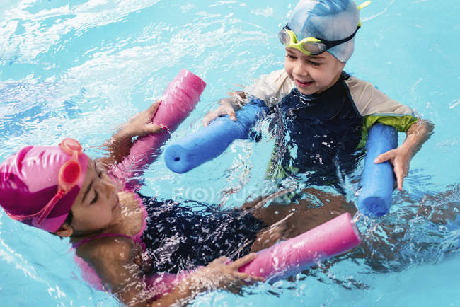 Niños alegres jugando con fideos de agua en la piscina . - foto de stock