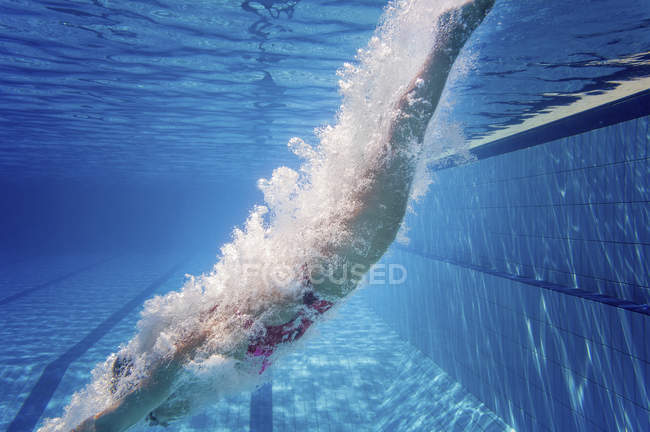 Nadadora hembra sumergiéndose en agua de piscina pública . - foto de stock