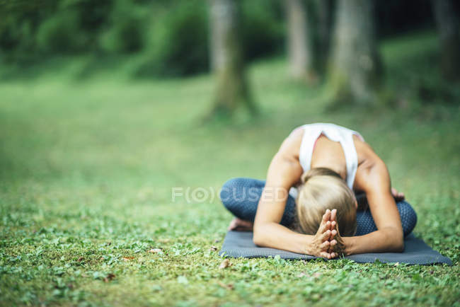 Mulher fazendo ioga, praticando sentado curva para a frente no tapete no parque . — Fotografia de Stock