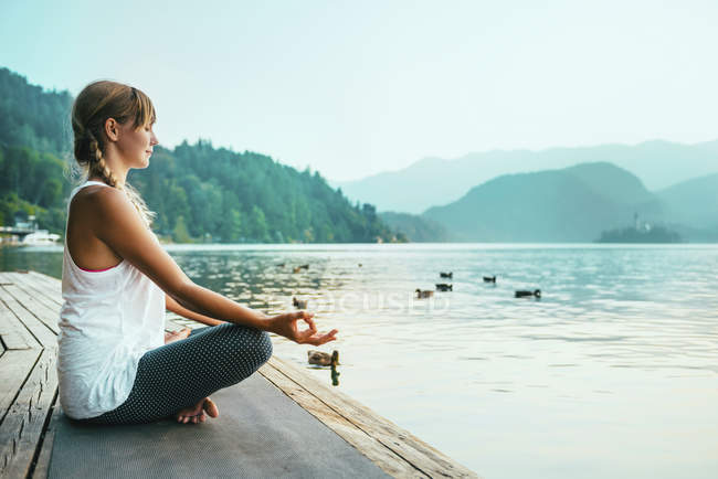 Жінка в позиції йоги лотоса, роздумуючи на озері на заході сонця . — стокове фото