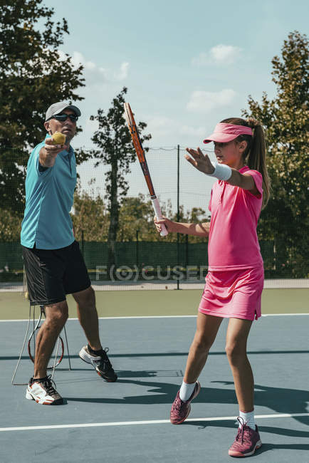 Male tennis instructor training teenage female player on court. — Stock Photo