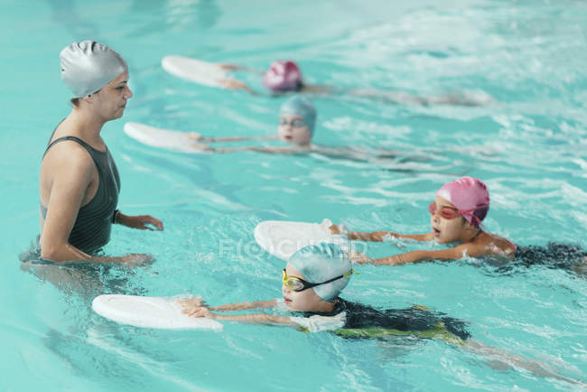 Swimming instructor with children using kicking boards in swimming pool. — Stock Photo