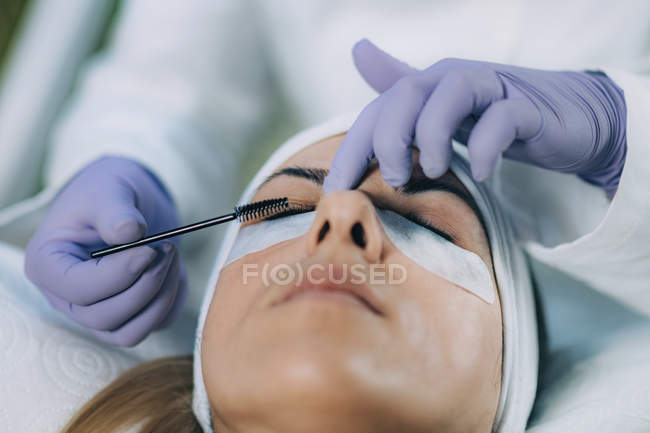 Cosmetologist curling eyelashes of patient and using curler in lash lifting procedure. — Stock Photo