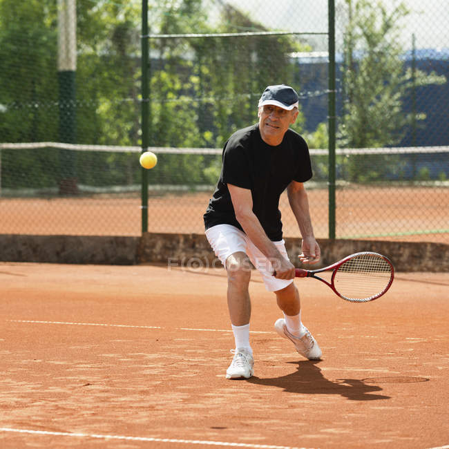 Homem sênior batendo bola no campo de ténis . — Fotografia de Stock