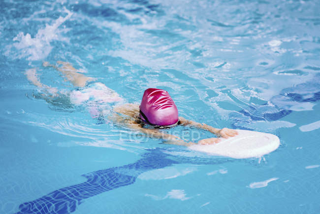 Menina aprendendo a nadar com prancha de pontapé na água da piscina . — Fotografia de Stock