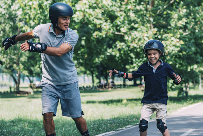 Carrera de patinaje con abuelo y nieto divirtiéndose en el parque . - foto de stock