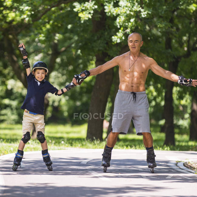Мальчик учится кататься на роликах с дедушкой в парке . — стоковое фото