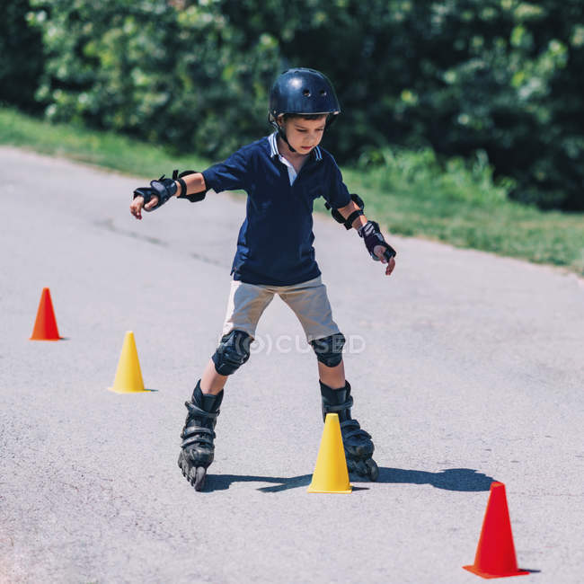 Мальчик тренируется кататься на роликах в парке на дороге с конусами . — стоковое фото