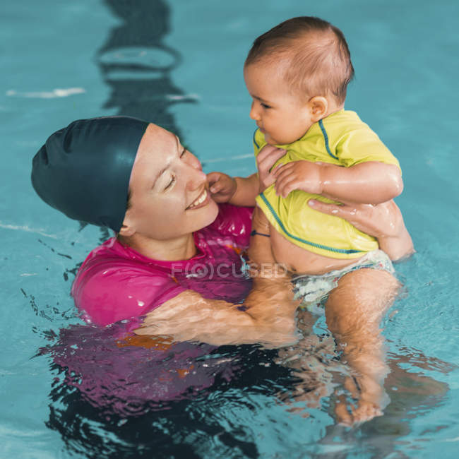 Female instructor holding baby boy with swimming class — Stock Photo
