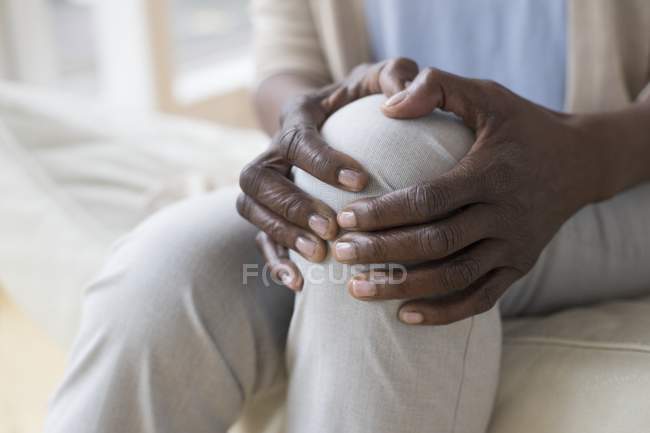 Close-up de mãos de mulher madura segurando joelho dolorido . — Fotografia de Stock