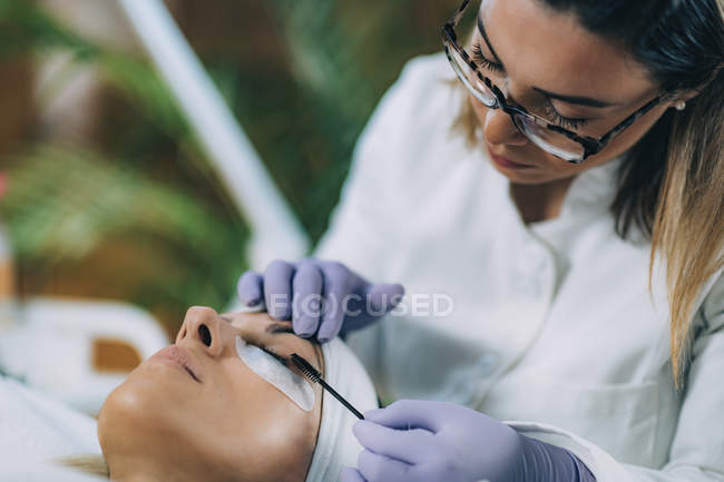 Cosmetologo curling ciglia del paziente e utilizzando bigodino nella procedura di sollevamento delle ciglia . — Foto stock