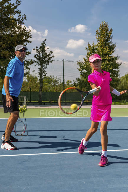 Entrenamiento de jugador de tenis adolescente con entrenador masculino en pista de tenis . - foto de stock