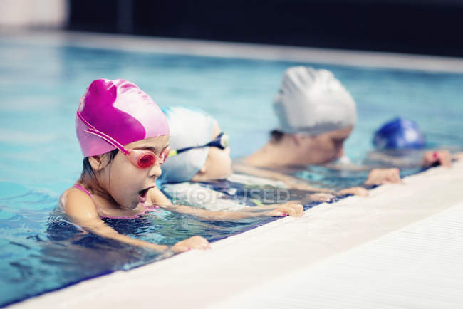 Niños con instructor de natación haciendo burbujas por borde de la piscina . - foto de stock