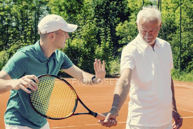 Senior activo practicando en clase de tenis con instructor masculino . - foto de stock