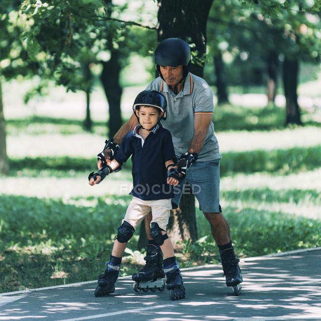 Nonno insegnamento nipote pattinaggio a rotelle nel parco estivo . — Foto stock